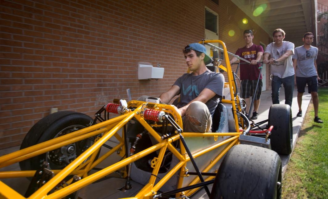Students roll their race car through campus to load it onto a trailer.