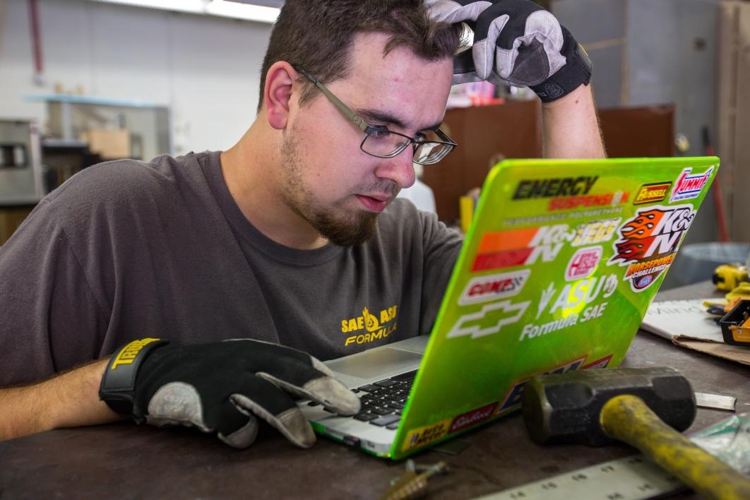 A student engineer works at a laptop in the Formula SAE club's shop.