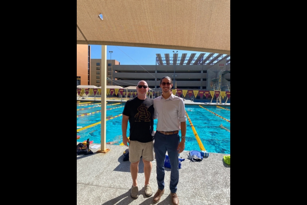 Two men stand in front of a pool posing for a photo.