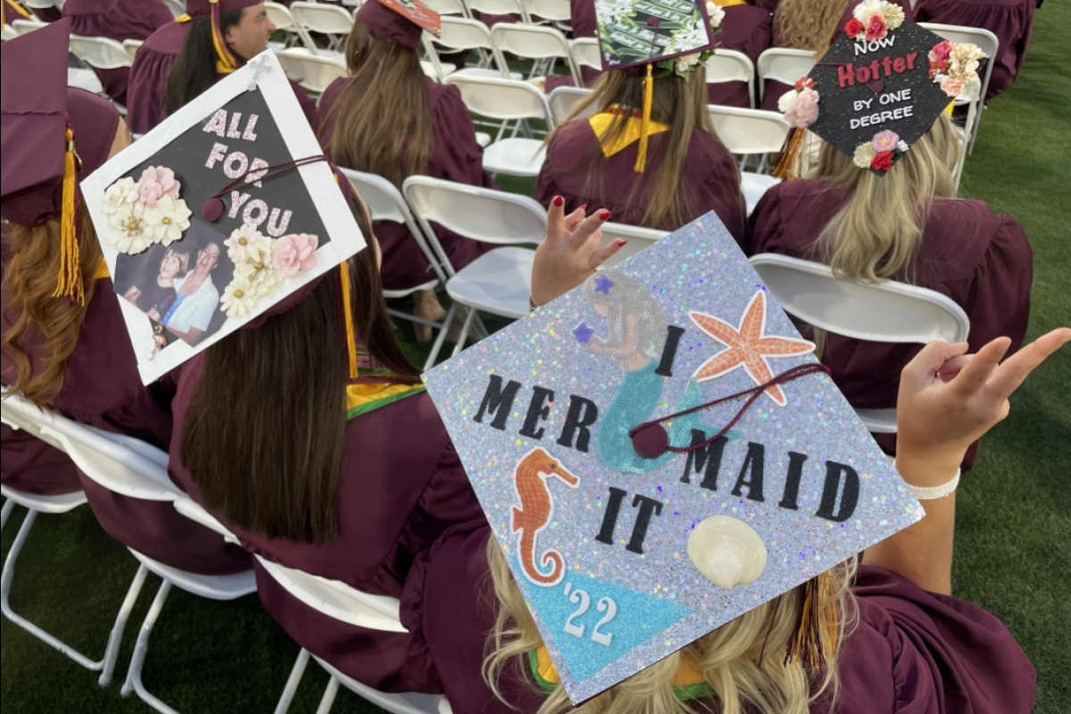 The back of two decorated grad caps, one reading I Mermaid It and the other saying All for You with a photo fo the grad's late mother