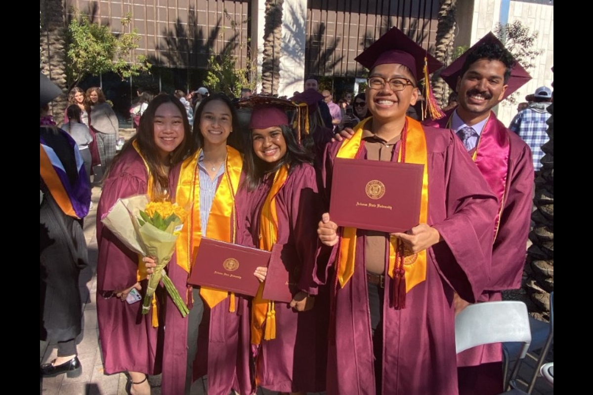 New grads in their maroon graduation caps and gowns smile as they hold their diploma covers following convocation