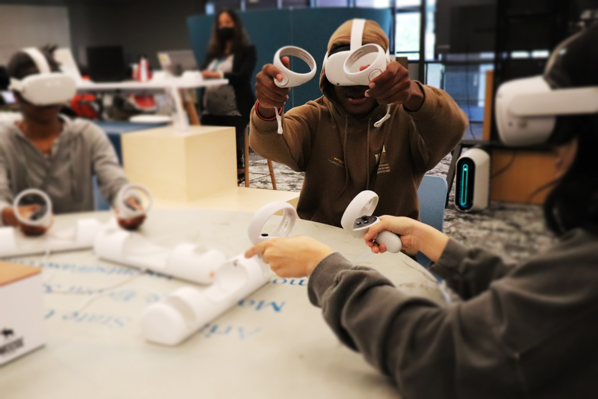 Students sit around a table wearing virtual reality headsets and handheld controllers
