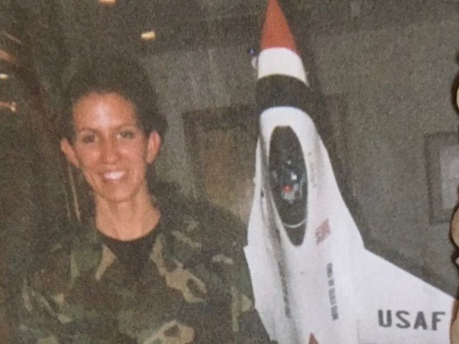Woman in Air Force poses in front of an F-16 Fighting Falcon model in 1999