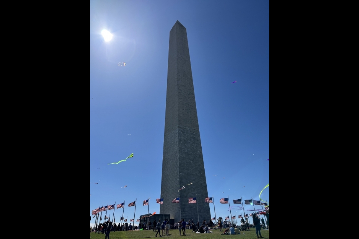 The Washington Monument against a blue sky with the sun shining in the corner.