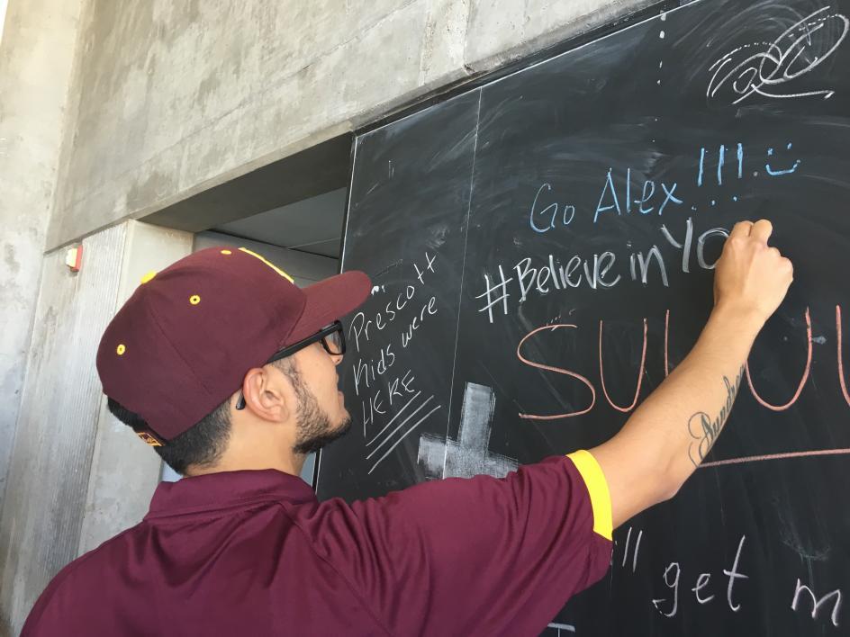student writing on outdoor chalkboard