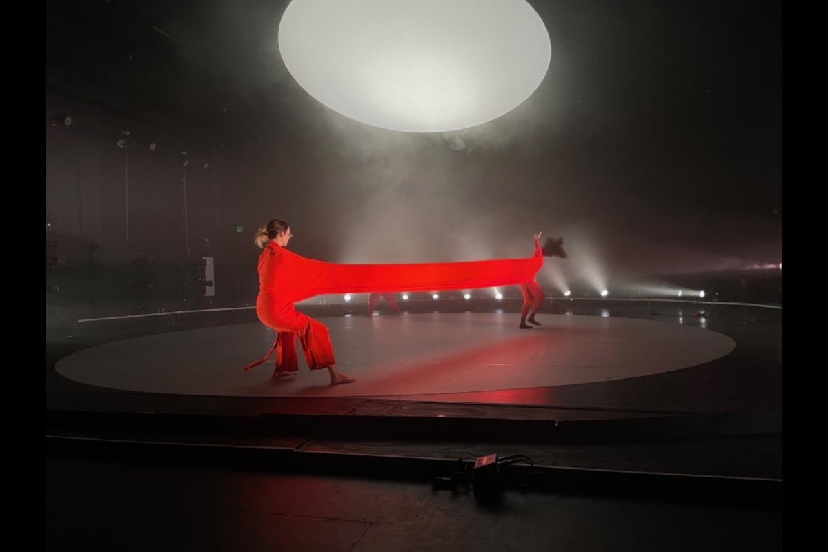 Two performers sharing a red costume, stretching it across stage.