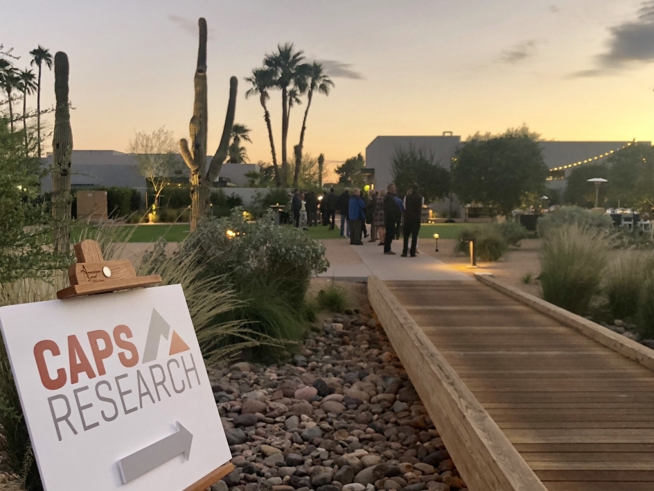 CAPS Research sign in foreground, people at outdoor networking event in background