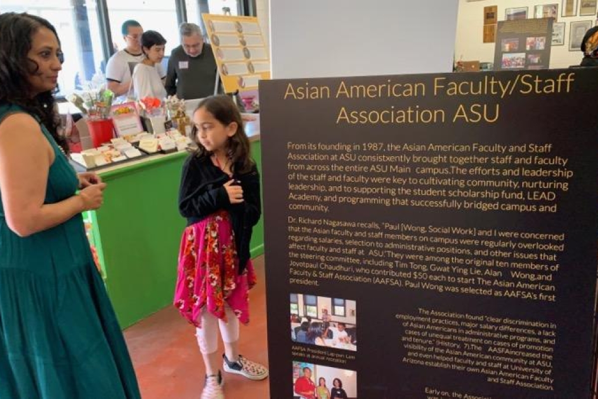 Person and child standing by a sign that reads "Asian American Faculty/Staff Association ASU"