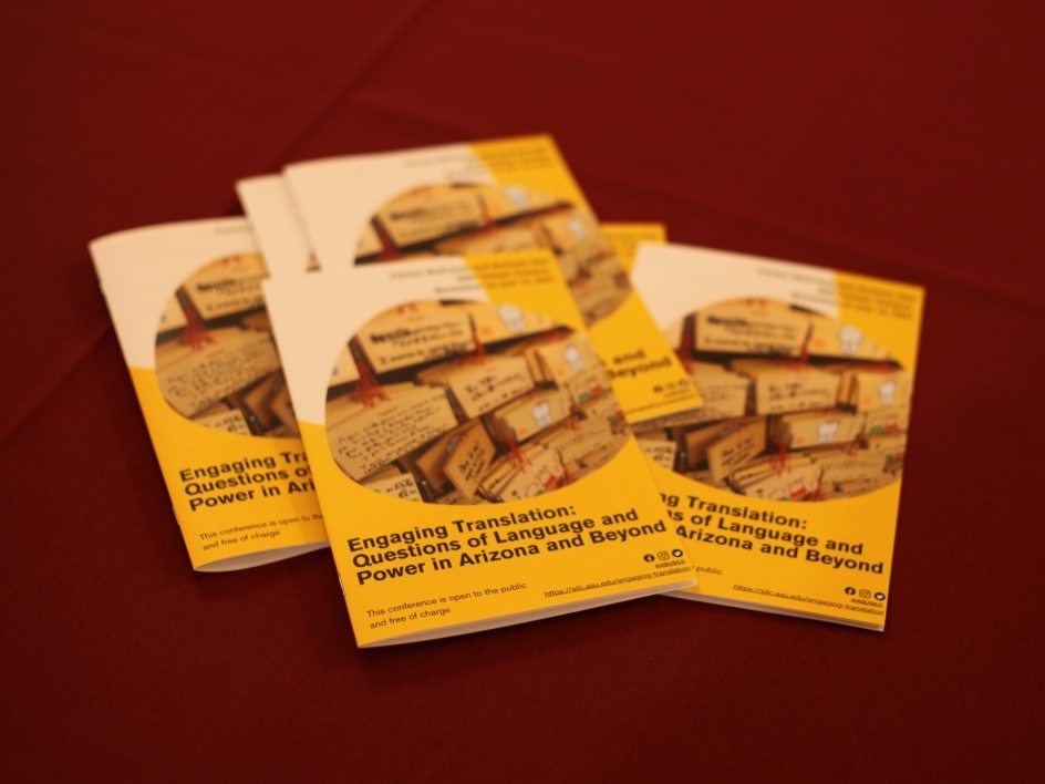A pile of five or six folded gold and white conference programs lie on top of a maroon tablecloth.