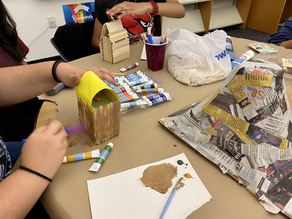 Emerson student painting a diorama with other art supplies on the table.