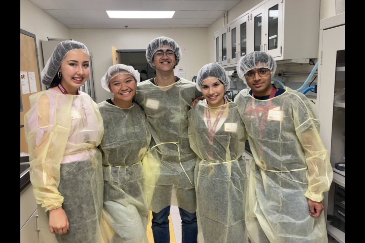 Group of five high school students wearing surgical coverings smile and pose for a group photo.