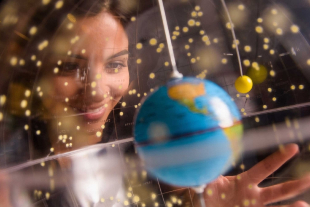 A woman looks through a clear globe at a small Earth