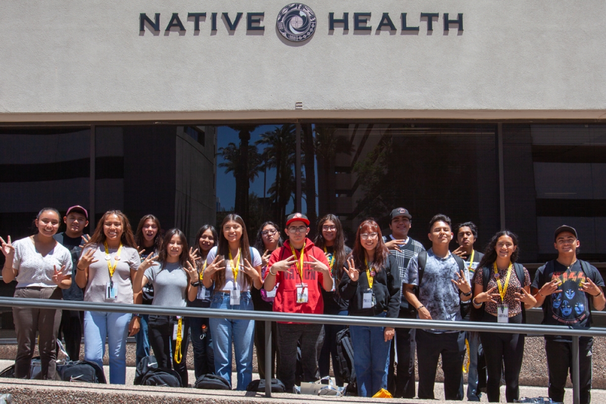 Group of American Indian high school students smiling and looking toward the camera outside of Native Health clinic.