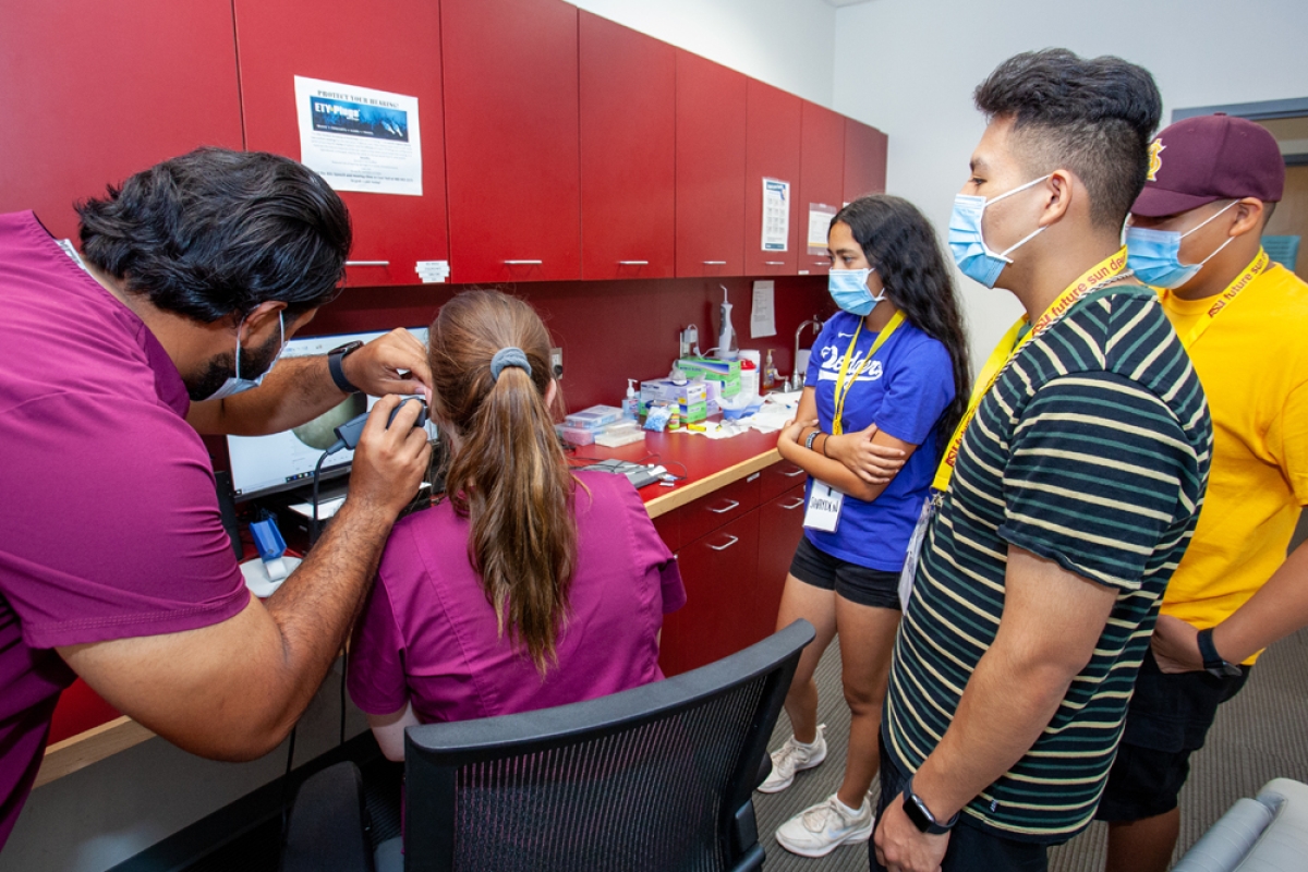 Three American Indian high school students watch as a clinician performs a hearing test on a patient.