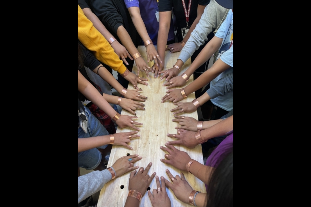 Hands are gathered in the middle of a table displaying metal rings and bracelets.