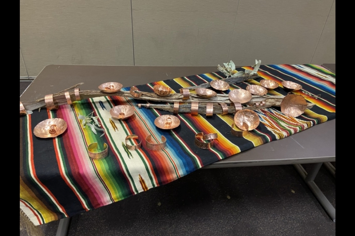 Metal rings, bracelets and bowls are displayed on a traditional cloth