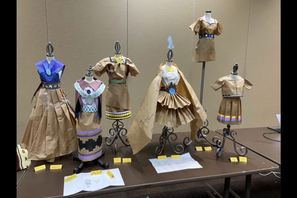 Paper regalia, created by the students, is displayed on miniature dress forms.