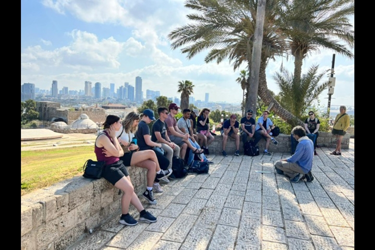 Students sit on a wall with the Tel Aviv skyline behind them