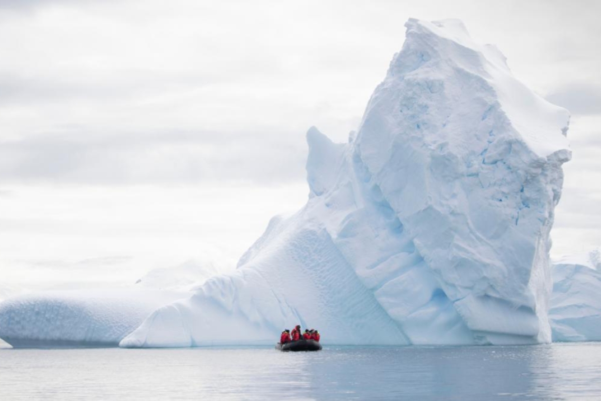 A zodiac boat off in the distance next to a large iceberg