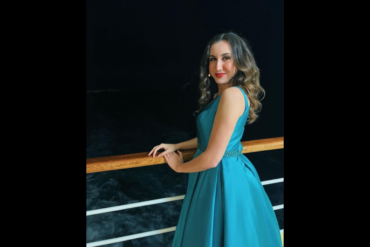 Woman in a blue dress leaning against a railing on a ship deck.