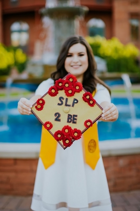 woman holding graduation cap that says "SLP 2 BE"