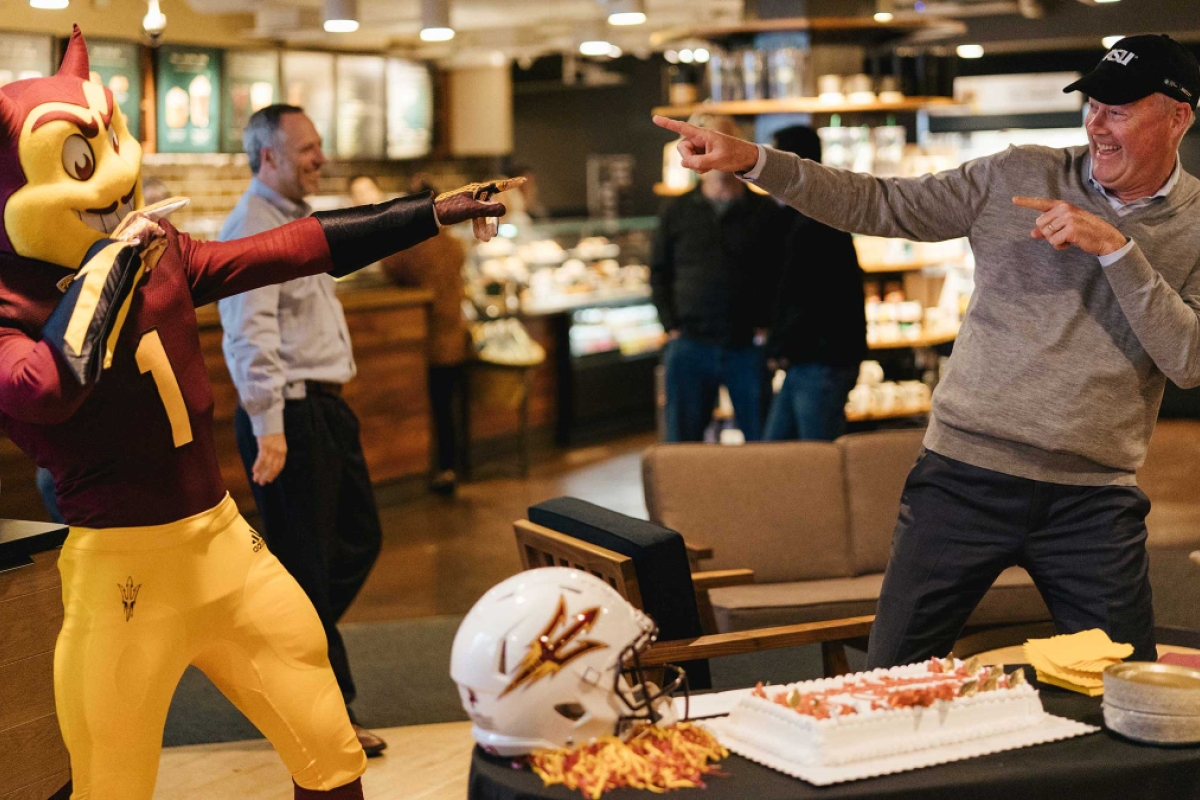 Sparky and Starbucks CEO Kevin Johnson point at each other at a fifth-anniversary celebration