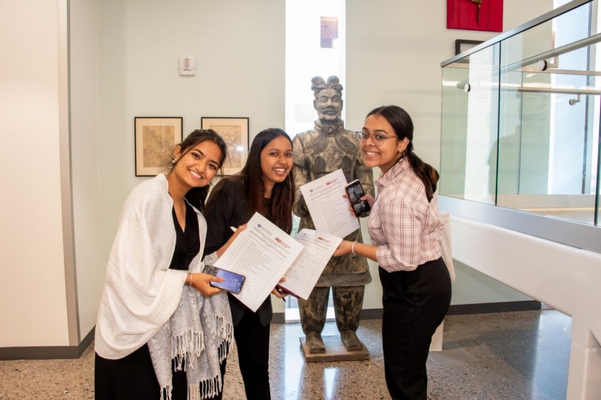 Three women smile and hold up paper documents.