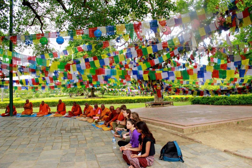 Students sit with Nepali monks under colorful flags
