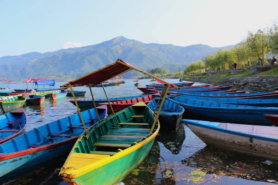 Boats sit in Nepali lake with mountains in background