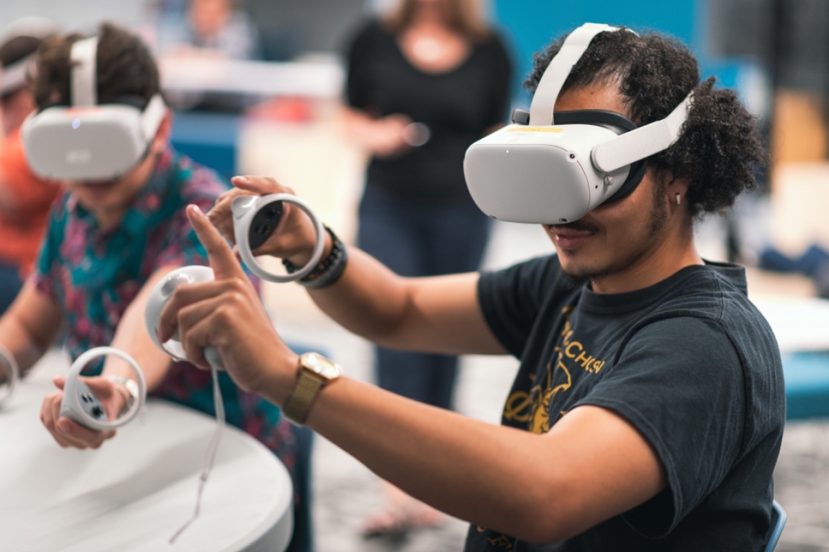 Student sitting with virtual reality headset on and his hands in the air, holding controllers 