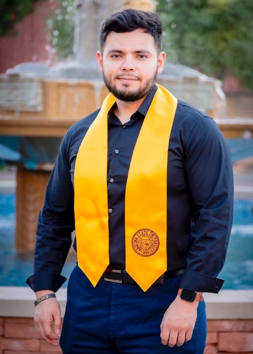 ASU College of Health Solutions graduate Alejandro Lopez wearing a gold sash and standing in front of the fountain at Old Main on ASU's Tempe campus