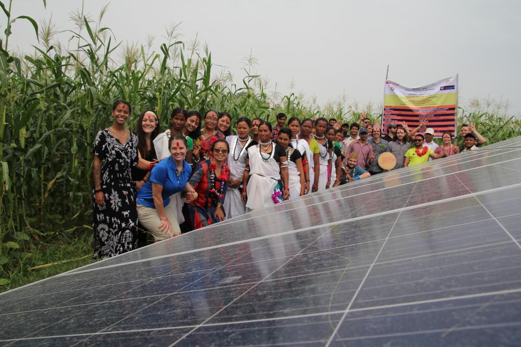 Students stand with Nepali community members next to solar panels
