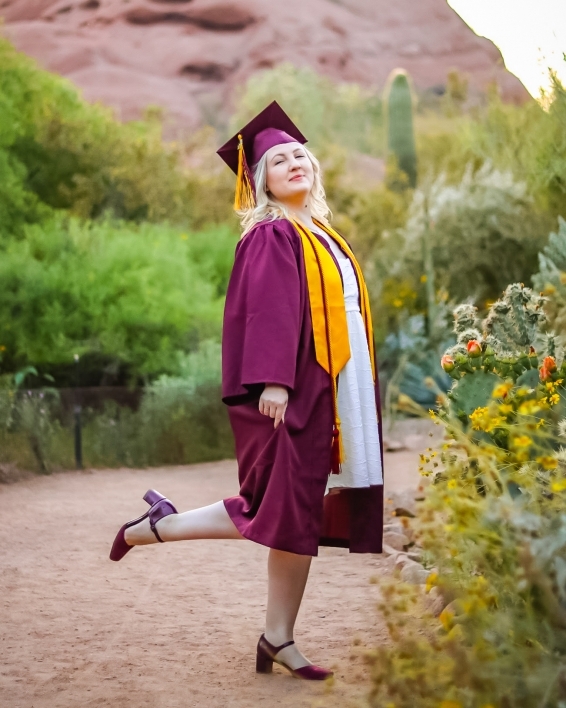 ASU College of Health Solutions graduate Evan Miller wearing her cap and gown while kicking one foot out behind her as she stands in a desert landscape