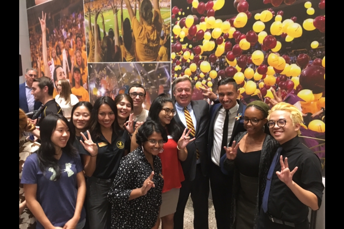 ASU President Michael Crow poses with a group of people making the ASU pitchfork sign with ther hands.