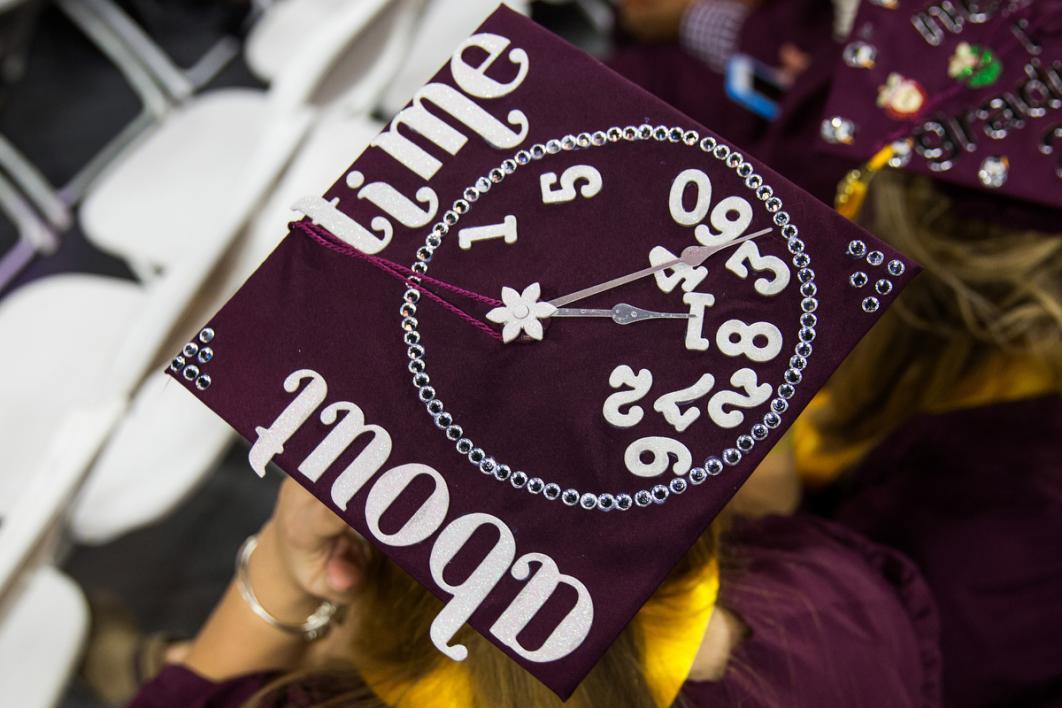 A graduation cap says, "About time," and all the clock face numbers are piled on the bottom of the cap