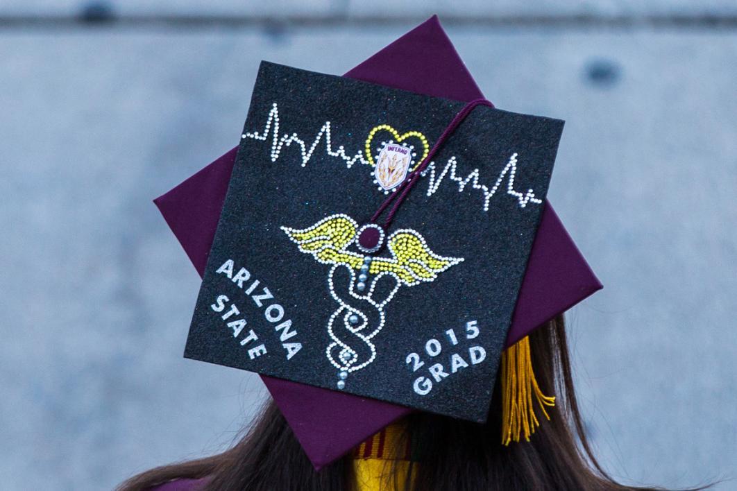 A graduation cap shows a caduceus, symbol of health professionals, in glitter with a heart beat behind it