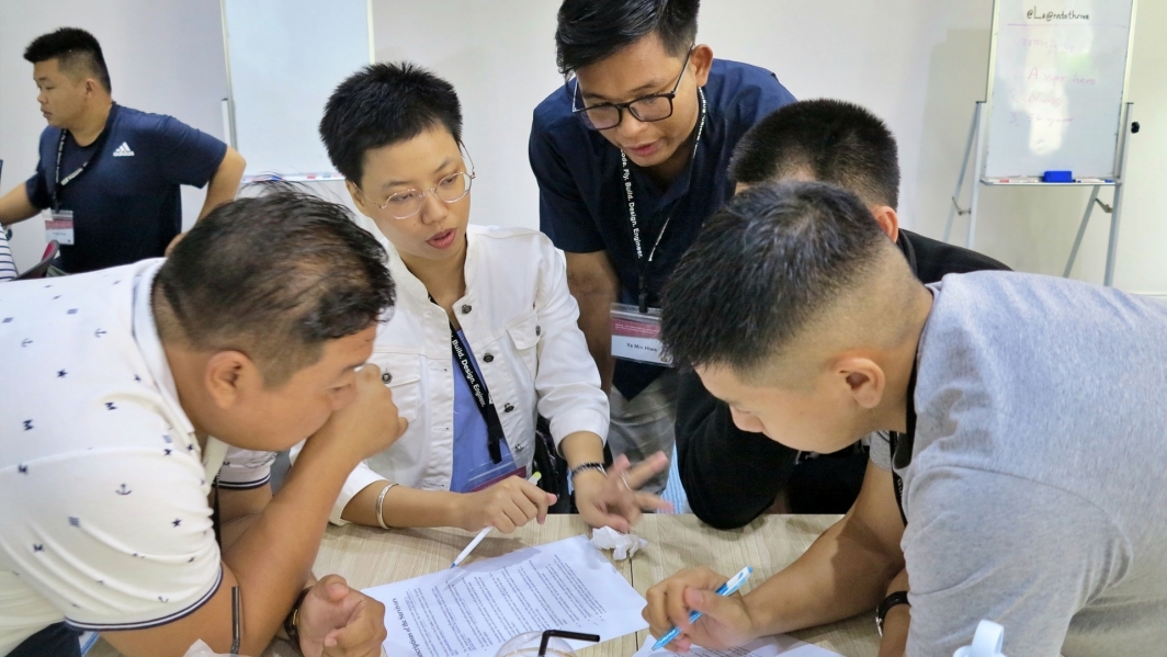 A small group of people from the Mekong-U.S. Partnership Young Scientist Program collaborate at a table and write on a piece of paper.