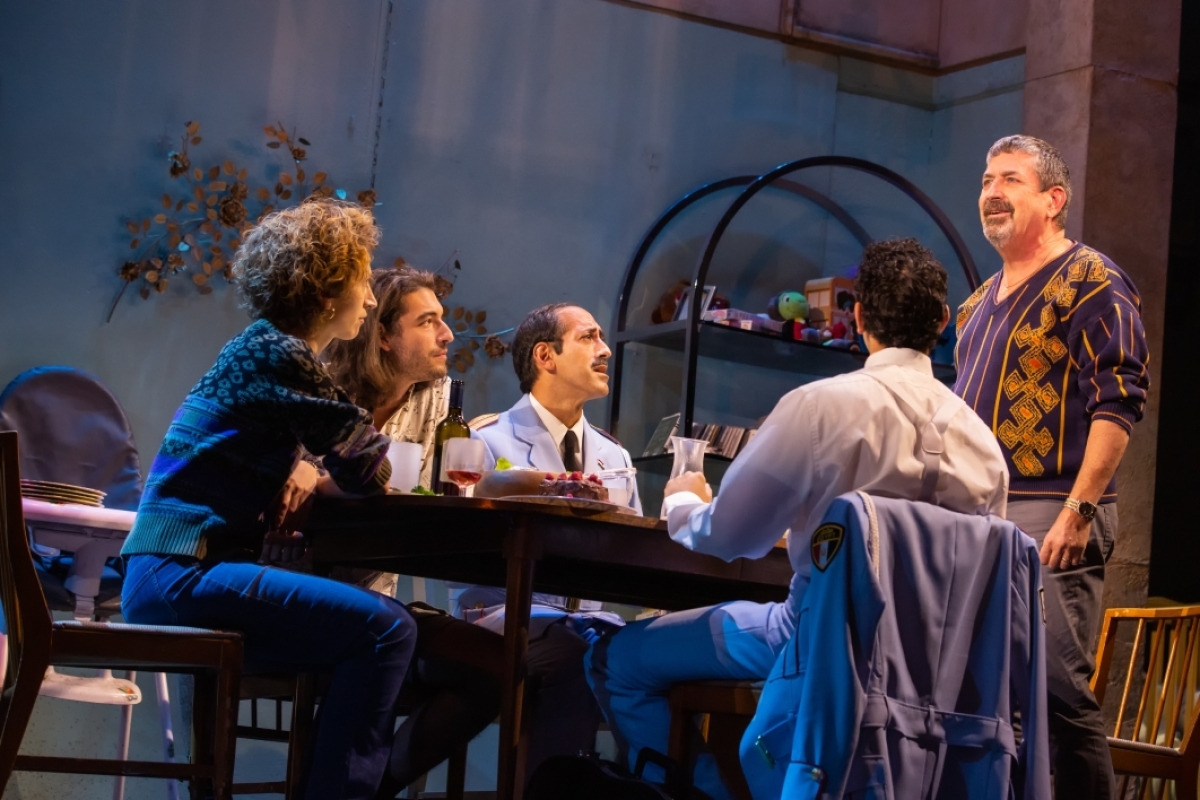 People seated around a table on stage in a scene from "The Band's Visit."