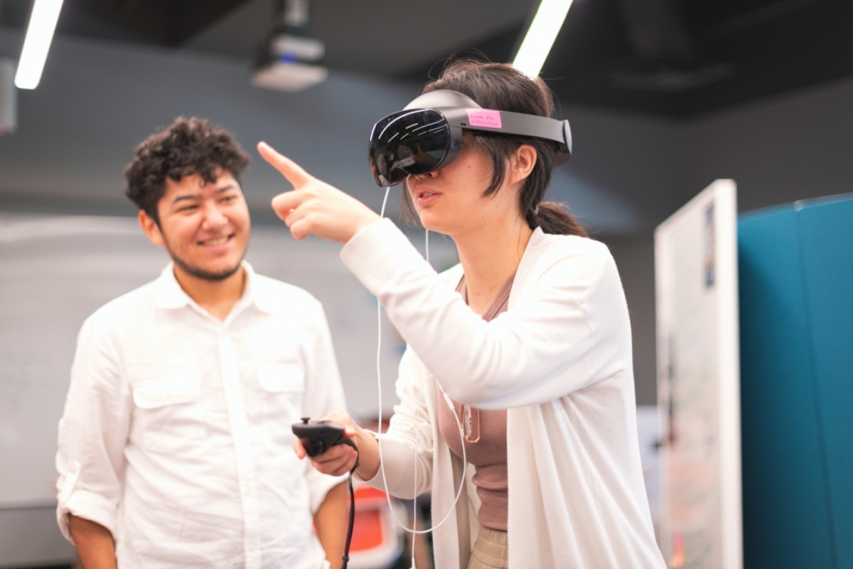 Students standing, with one wearing a virtual reality headset