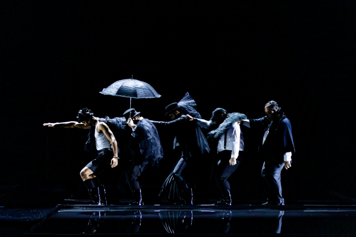 A line of people on a stage dance in water.