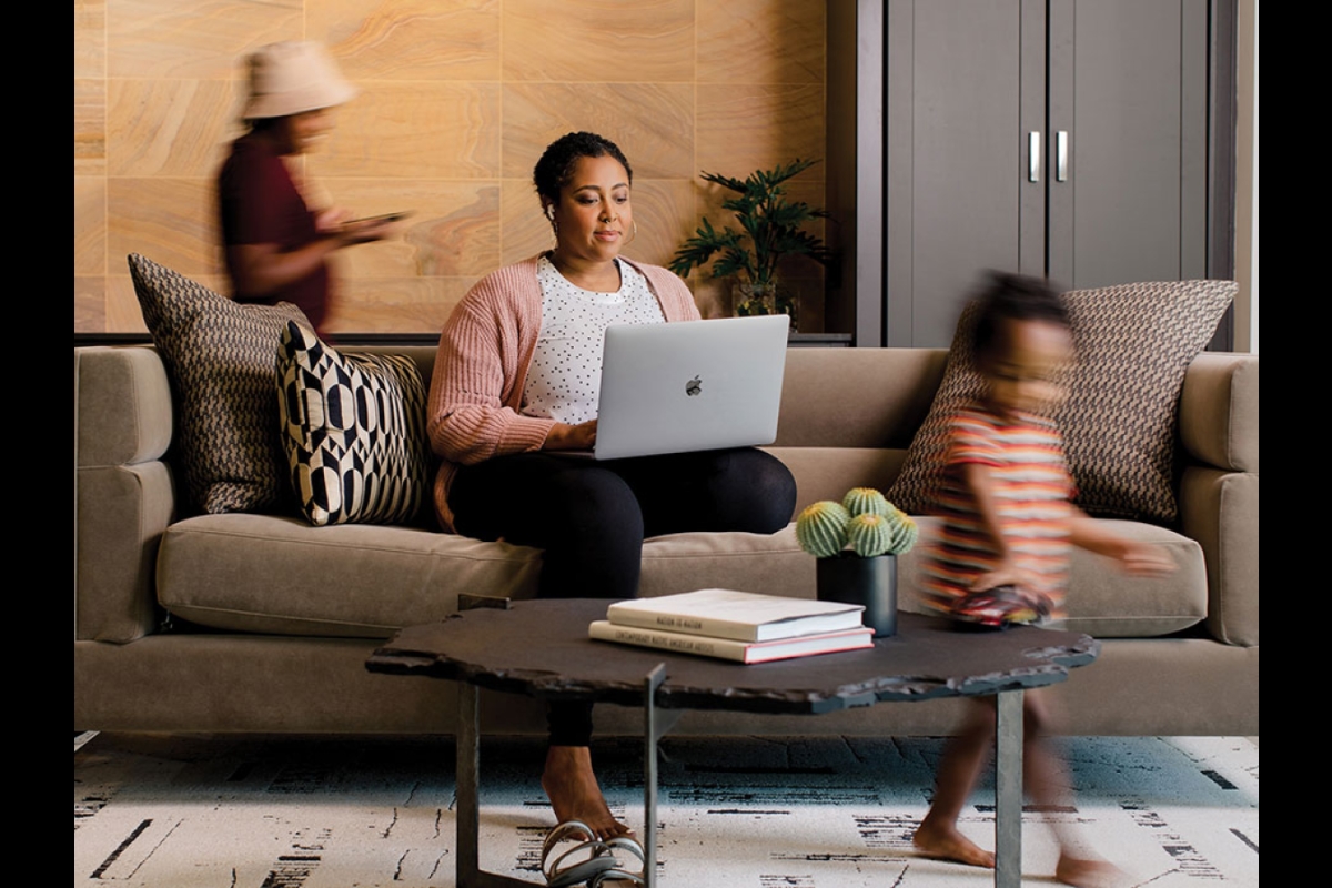 woman sitting on couch on laptop with family walking around her