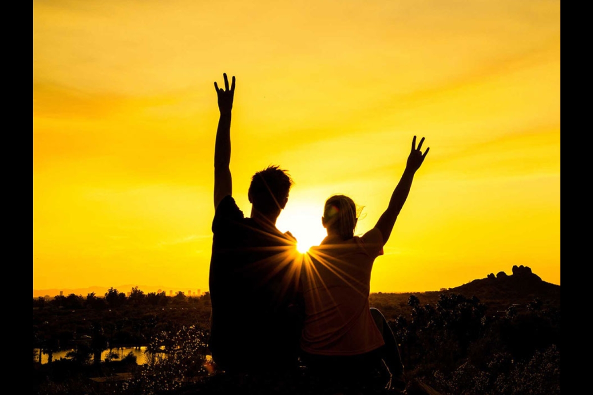 two people with arms raised making pitchfork sign with sun behind them