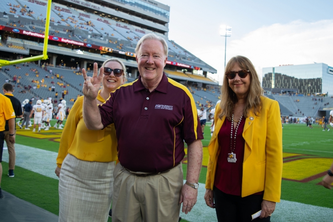 A man flanked by two women flashes the pitchfork at the edge of the ASU football field