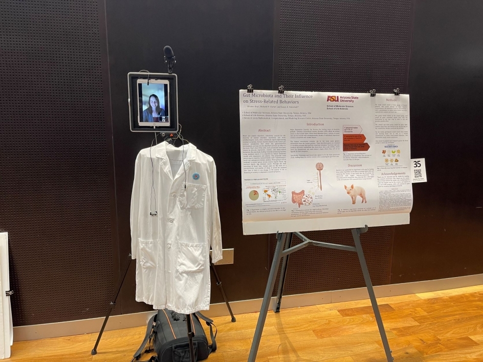 An online student's poster presentation featuring a poster on an easel, an Ipad on a stand with a podcast microphone, and a lab coat hanging under the Ipad