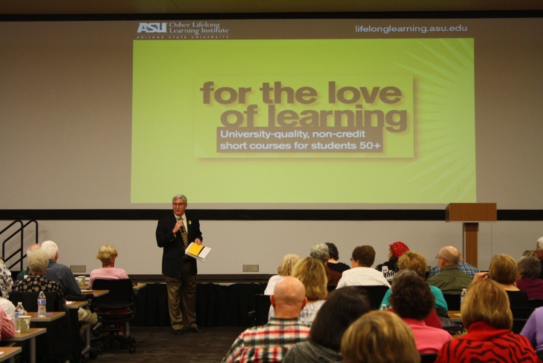 Richard Knopf stands in front of a presentation that reads "for the love of learning" and a group of people sitting down.