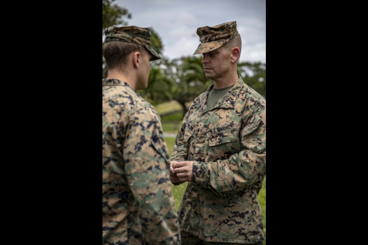 Man wearing military fatigues bestowing an award on another man wearing military fatigues.