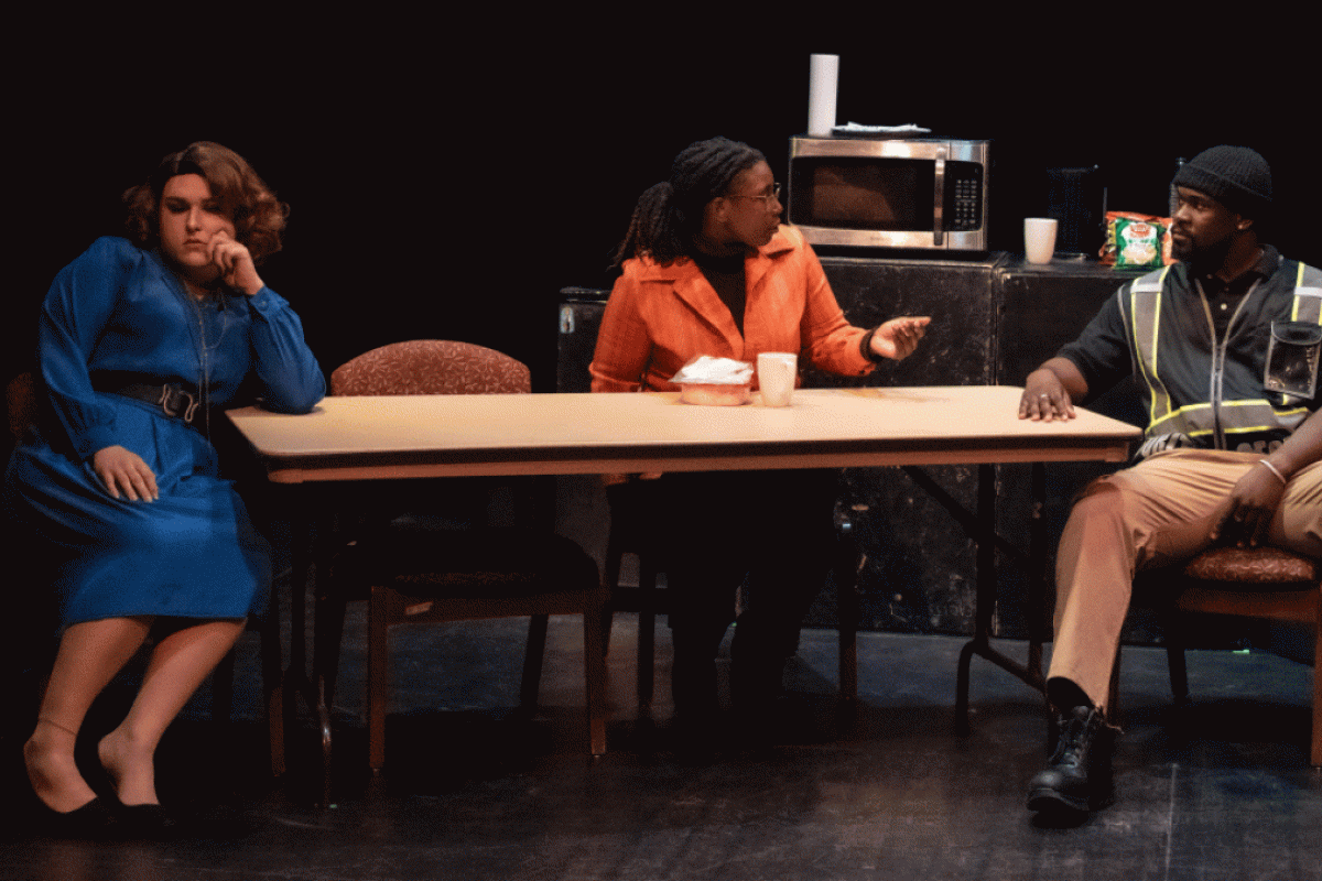 People seated at a table on a stage while acting in a play.