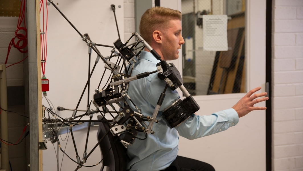 A student demonstrates a wearable robotic-aided rehabilitation framework on his shoulder for exercise therapy.