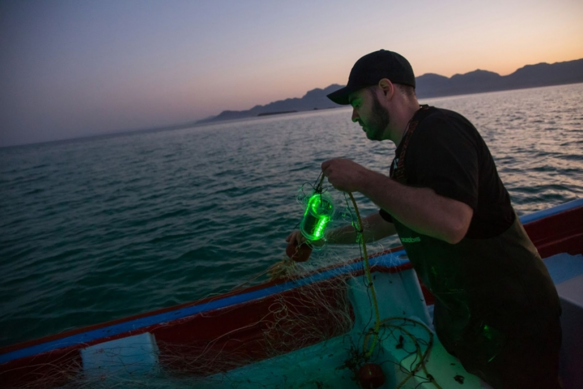Senko on a boat holding a lit up net in low light with ocean in the background