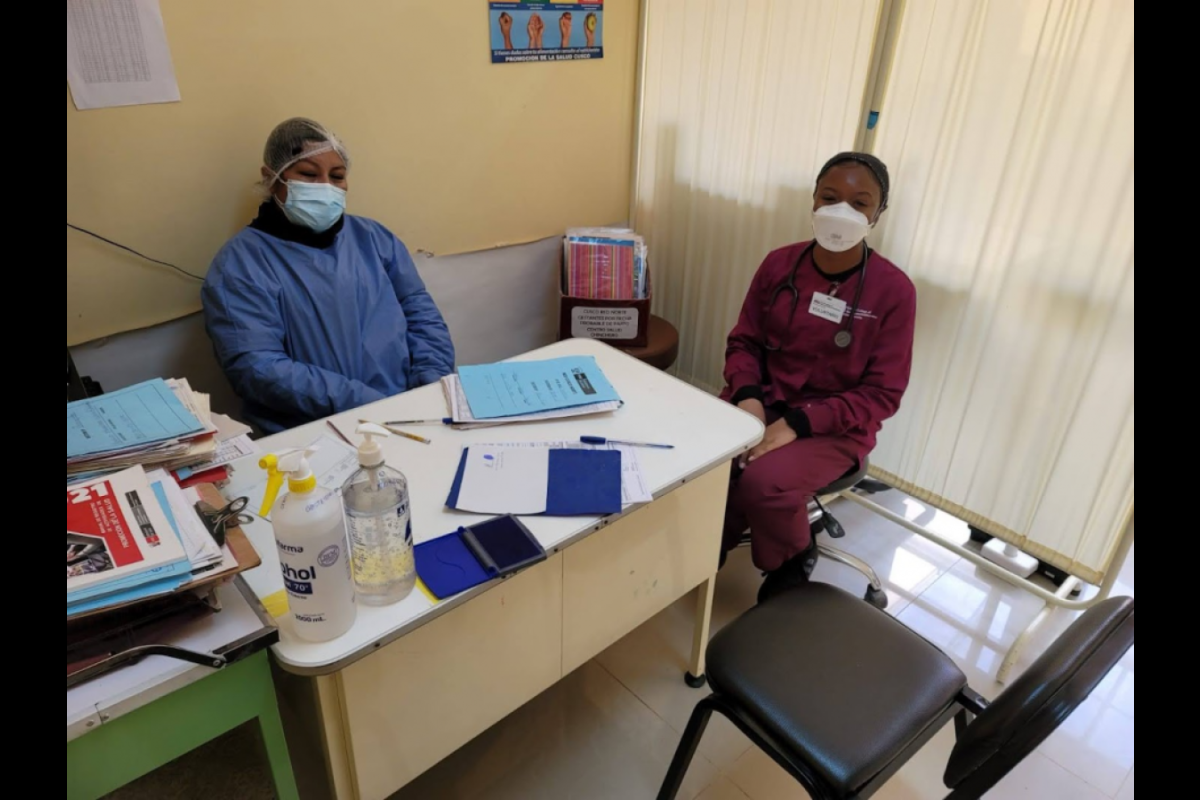 Shaniece Randolph shown in her maroon nursing student scrubs sitting next to a health care worker at a clinic in Peru